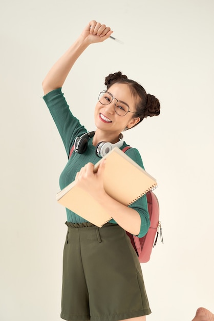 Aluna linda usando uma mochila segurando um caderno sobre um fundo branco isolado