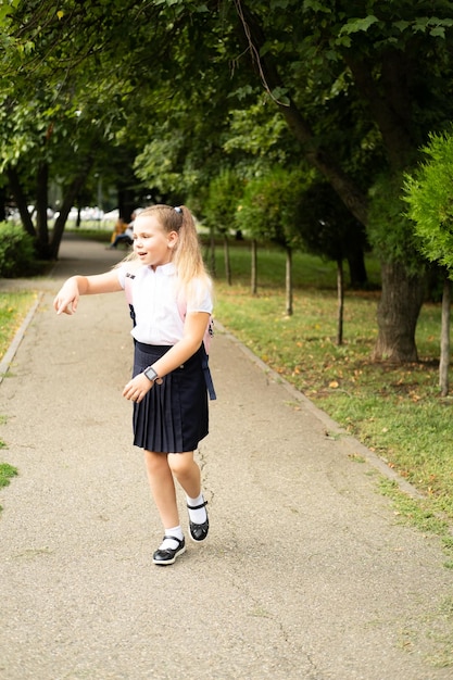 Aluna loira sorridente em uniforme escolar com mochila rosa indo para a escola ao ar livre