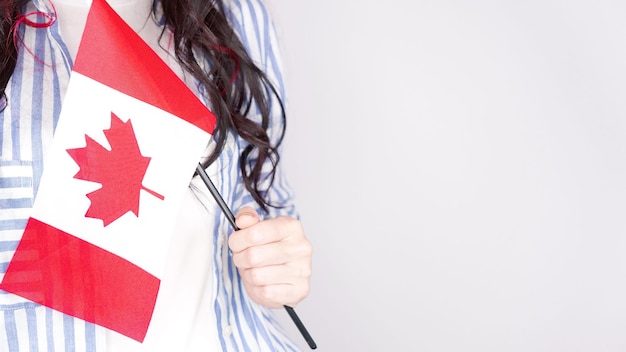 Aluna não reconhecida em camisa azul branca segurando pequena bandeira canadense sobre o dia cinza do Canadá