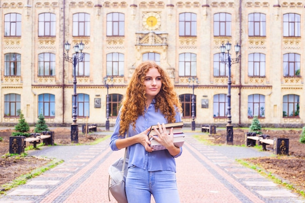 Aluna ruiva com uma pilha de livros provenientes da biblioteca da universidade