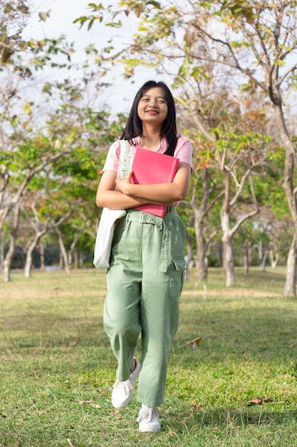 Aluna segurando livro e caminhando no parque verde