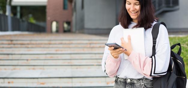 Aluna segurando um smartphone e um bloco de notas