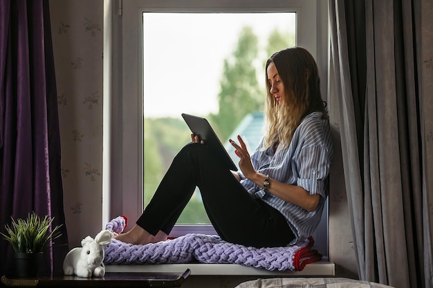 aluna senta-se no parapeito da janela da sala e estuda online no tablet