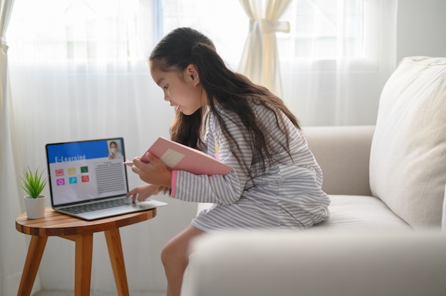 Aluna sentada à mesa, escrevendo a lição de casa. Adolescente que usa o laptop para estudar. Novo normal. Distanciamento social. Fique em casa.