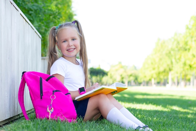 Aluna sentada na grama com uma mochila e um livro e sorri