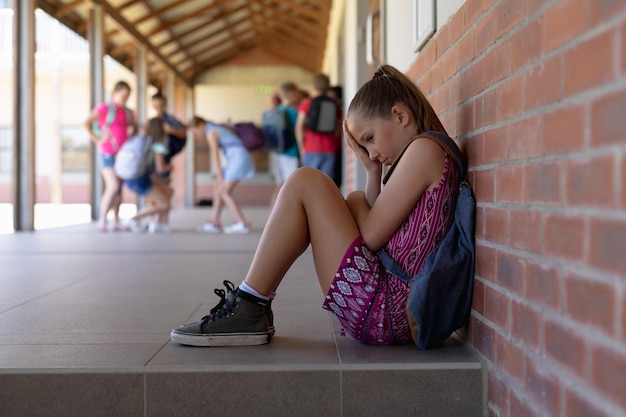 Foto aluna sentada no chão contra uma parede sozinha no pátio da escola primária