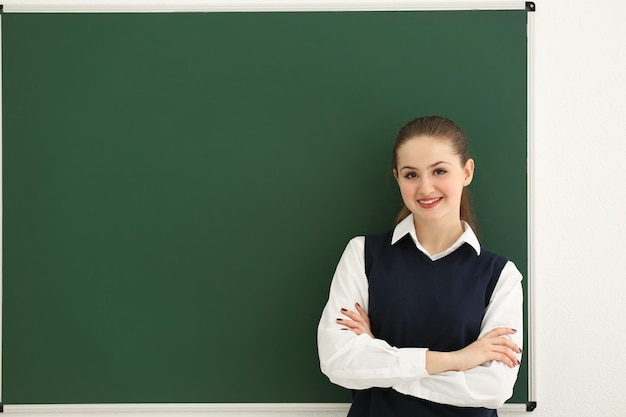 Aluna sorridente com os braços cruzados em pé no quadro-negro na sala de aula