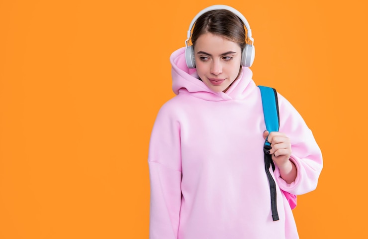 Foto aluna sorridente em fones de ouvido com mochila em fundo amarelo