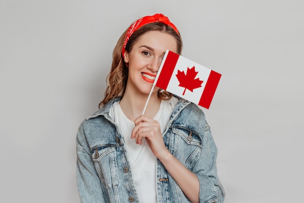 Aluna sorrindo e cobrindo metade do rosto com uma pequena bandeira do Canadá isolada sobre um fundo branco, dia do Canadá, feriado, aniversário da confederação, cópia espaço