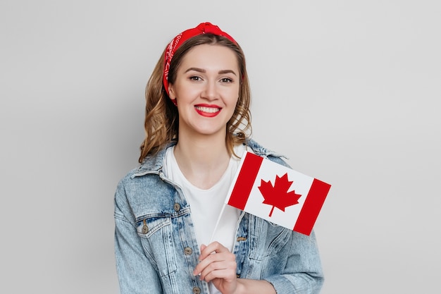 Aluna sorrindo e segurando uma pequena bandeira do Canadá isolada sobre uma parede cinza, dia do Canadá, feriado, aniversário da confederação, cópia espaço