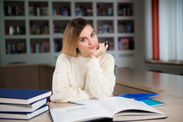 Aluna tomando notas de um livro na biblioteca. Jovem mulher sentada à mesa, fazendo atribuições na biblioteca da faculdade.