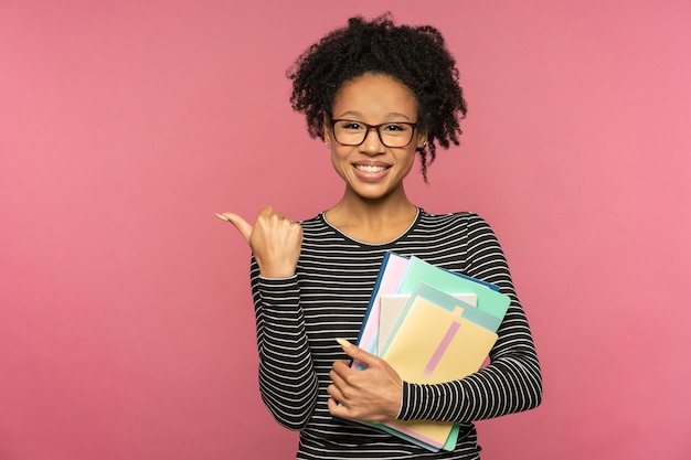 Aluna usando óculos segurando cadernos sorrindo, mostrando o dedo no espaço livre