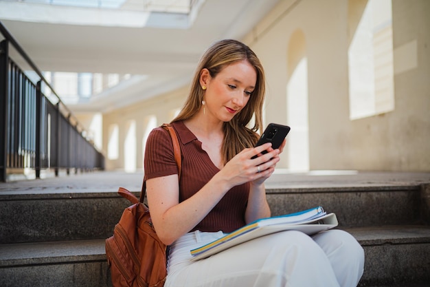 Aluna verificando seu telefone enquanto ela está sentada nas escadas do campus universitário