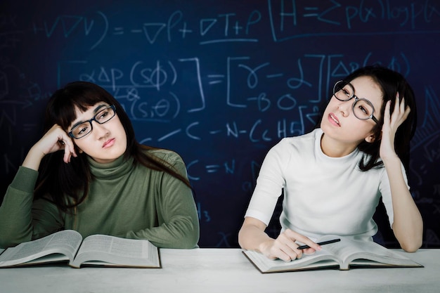 Alunas entediadas na mesa com fórmula matemática no fundo do quadro-negro