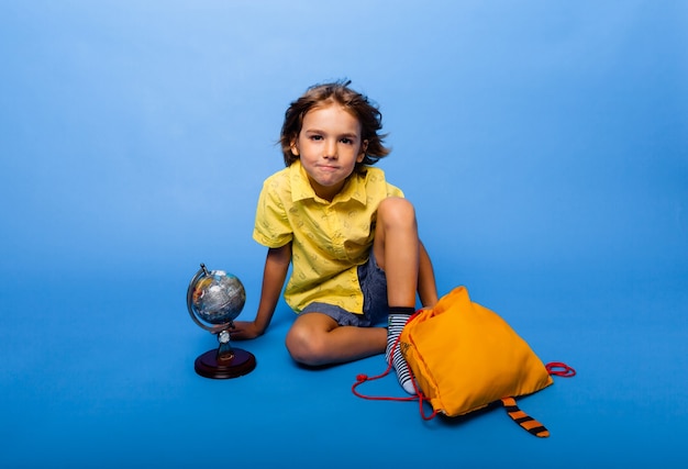 Aluno alegre senta-se sobre um fundo azul com uma mochila e um globo. conceito de educação