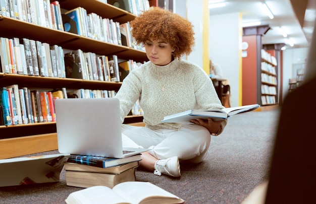 Aluno aprendendo pesquisa de laptop e mulher negra na biblioteca trabalhando no chão com livros Lendo pesquisa de computador e estudo on-line de uma pessoa com informações de teste e exame para a universidade