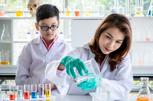 Aluno asiático atento observando a tutora despejando líquido em frascos enquanto conduzia um experimento com reagentes coloridos durante a aula de química no laboratório.