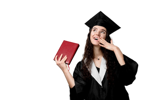 Aluno com livro no manto de formatura e boné pronto para terminar a faculdade. Jovem acadêmica em vestido preto sorrindo.