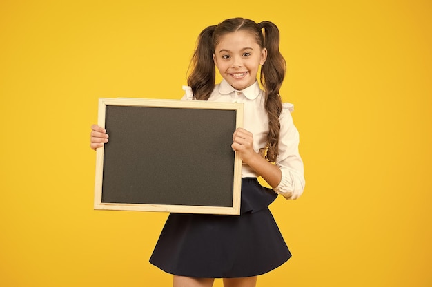 Aluno da escola informando a você A menina da escola segura o espaço da cópia do quadro-negro em branco Anúncio e promoção Confira isso Uniforme escolar da menina segure o quadro-negro De volta ao conceito da escola Não se esqueça