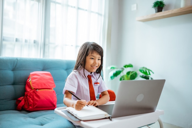 Aluno da primeira série com uniforme durante o estudo da aula online com o professor em casa