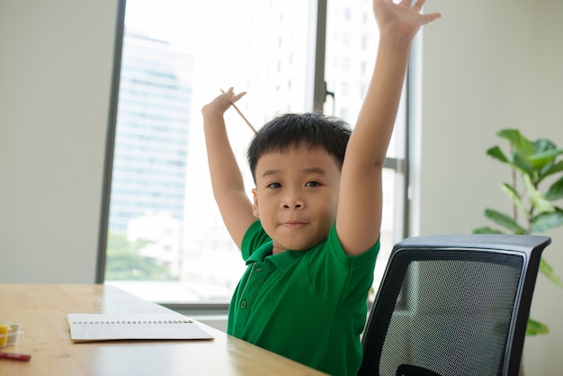 Aluno da Ásia estudando e fazendo a lição de casa em casa, na mesa, educação em casa, pensando em ação