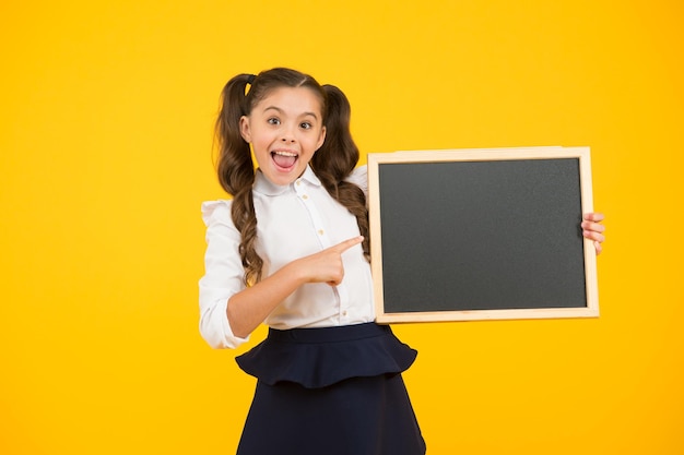 Aluno de estudante cabelos longos informando a você A garota da escola segura o espaço em branco da cópia do quadro-negro Anúncio e promoção Confira isso Uniforme escolar da garota segura o quadro-negro De volta ao conceito da escola