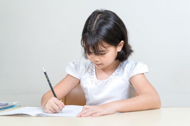 Aluno de meninas asiáticas escrevendo em um caderno fazendo lição de casa e fazendo autoestudo em casa