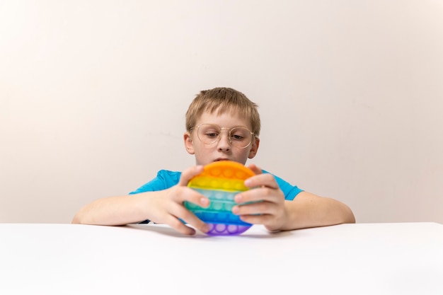 Aluno de óculos joga pop-lo brinquedo em uma mesa branca e fundo de parede branco