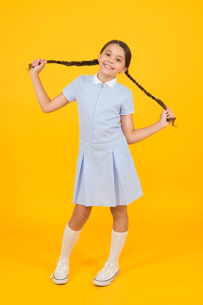 Aluno despreocupado menina pequena em uniforme escolar olhar retrô criança em estilo vintage moda infantil da velha escola criança feliz em fundo amarelo moda e beleza infância felicidade humor engraçado