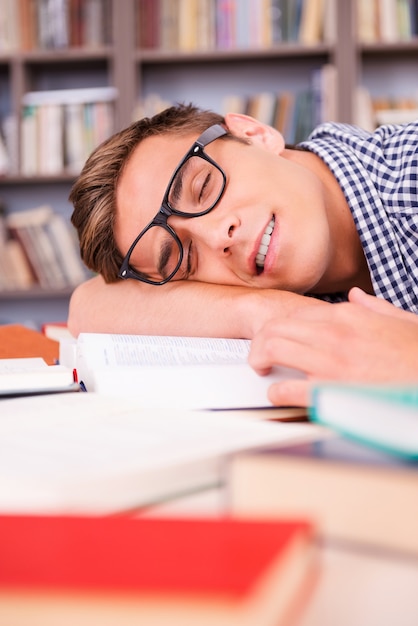 Aluno dormindo. jovem bonito dormindo sentado na biblioteca e apoiando o rosto na mesa