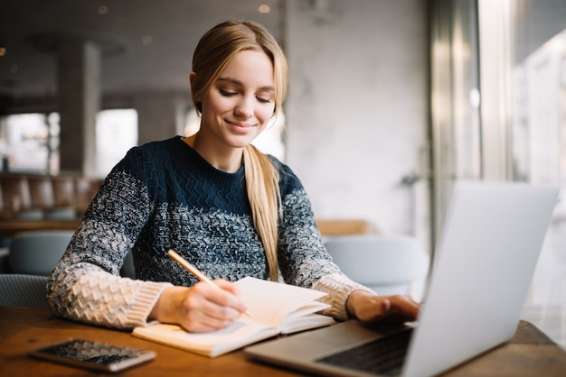 Aluno estudando, usando o computador portátil, educação on-line. Freelancer de mulher bonita escreve notas, planejando o projeto de trabalho, trabalhando em casa