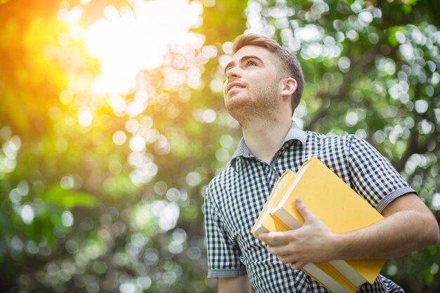 Aluno estudante branco sorrindo com livro amarelo no jardim