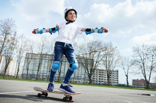 Aluno feliz e sorridente com equipamento de proteção e capacete mantém o equilíbrio enquanto anda de skate