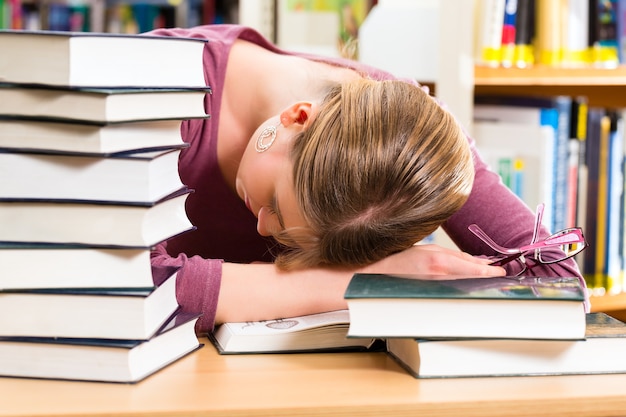 Aluno - Jovem na biblioteca com livros aprendendo, ela está dormindo, cansada e sobrecarregada de trabalho