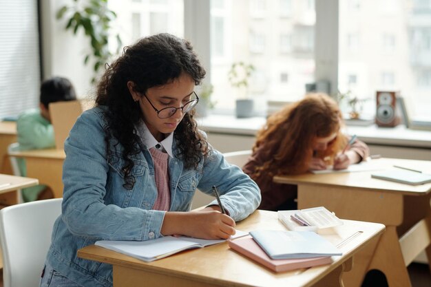 Aluno muito multiétnico em roupas casuais fazendo anotações no caderno na aula