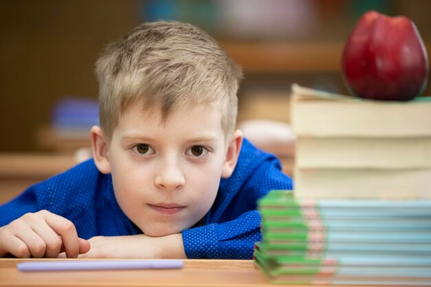 Aluno na mesa Menino na sala de aula com livros e uma maçã Escola secundária De volta à escola