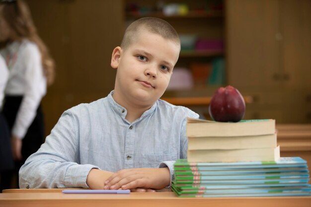 Aluno na mesa Menino na sala de aula com livros e uma maçã Escola secundária De volta à escola