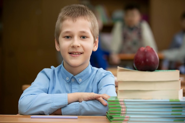 Aluno na mesa Menino na sala de aula com livros e uma maçã Escola secundária De volta à escola