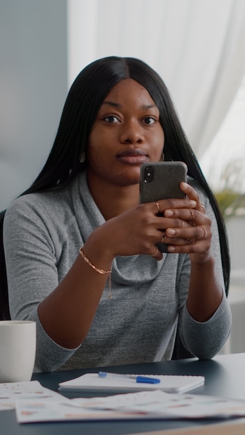 Aluno negro segurando o telefone nas mãos, conversando com pessoas que navegam por informações de comunicação, sentadas na mesa na sala de estar. adolescente procurando nas redes sociais, compartilhando conselhos sobre estilo de vida para amigos do grupo