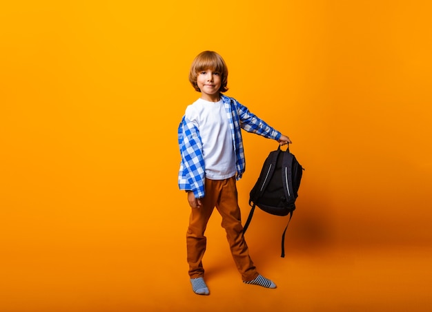 Aluno segura uma mochila isolada em um fundo amarelo.