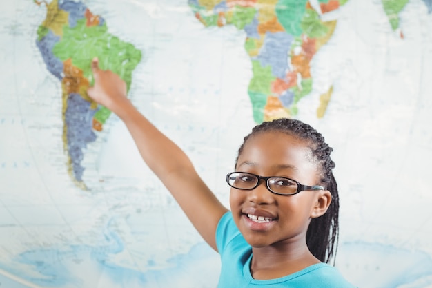 Aluno sorridente apontando no mapa do mundo em uma sala de aula