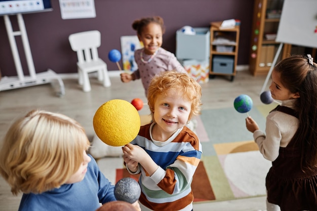 Aluno sorridente bonito da escola primária com modelo de sol olhando para a câmera em pé entre outros k