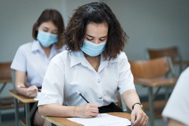 Alunos alegres na sala de aula usam máscaras protetoras e usam anti-séptico para prevenção do coronavírus durante a pandemia de coronavírus. Grupo de alunos usando máscaras de proteção em sala de aula.