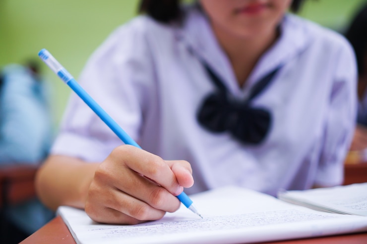 Foto alunos asiáticos segurando uma caneta em um uniforme escolar branco.