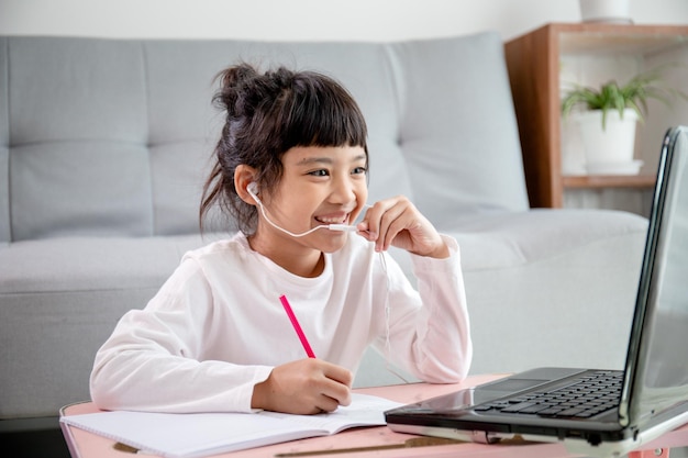 Alunos asiáticos usam fones de ouvido, estudam online com videochamada com o professor, Jovem feliz aprendendo ecologia terrestre ouvir palestra assistir escrever notas olhar para o laptop em casa. Coronavírus deovid-19.