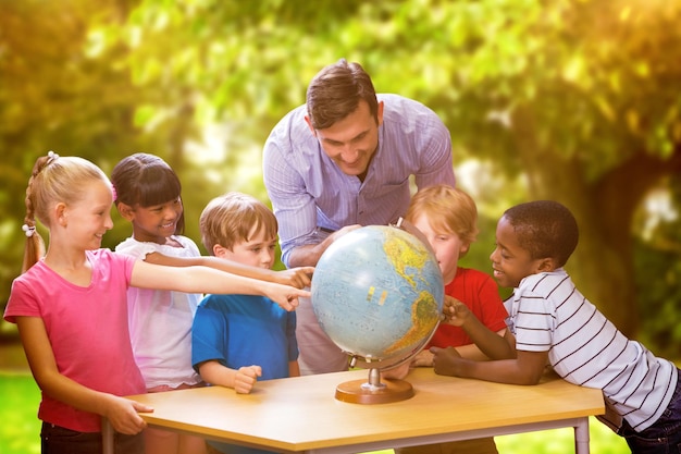 Alunos bonitos e professor olhando para o globo na biblioteca contra árvores e prados no parque