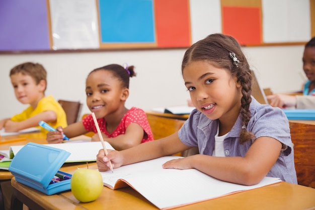 Alunos bonitos que escrevem na mesa na sala de aula