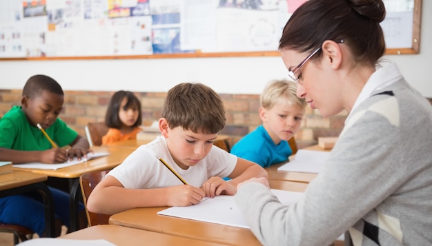 Alunos bonitos que escrevem na mesa na sala de aula