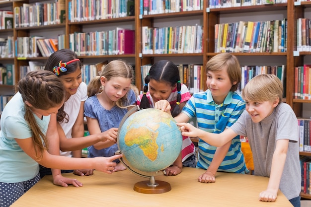 Alunos bonitos que olham o globo na biblioteca