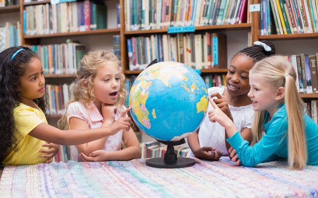 Alunos bonitos que olham o globo na biblioteca